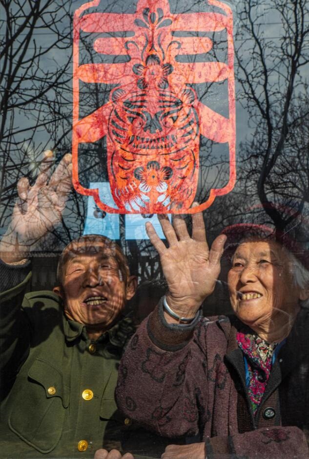 臘月里，霍州市師莊鄉(xiāng)馮南垣村村民師榮光(左)在災(zāi)后重建的新家里貼窗花。(霍州市委宣傳部供圖)