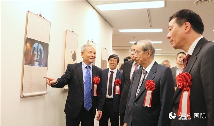 “湖州印象”攝影展主創(chuàng)、世界華人攝影協(xié)會副會長馮學(xué)敏向吳江浩大使、福田康夫前首相等嘉賓介紹展出作品。（人民網(wǎng) 許可攝）