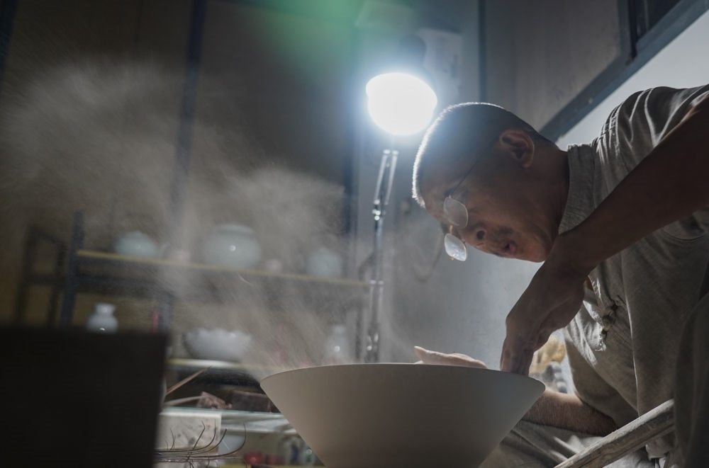 ↑ 在景德鎮(zhèn)，手工匠人吹去坯內(nèi)的泥土（2021年7月14日攝）。