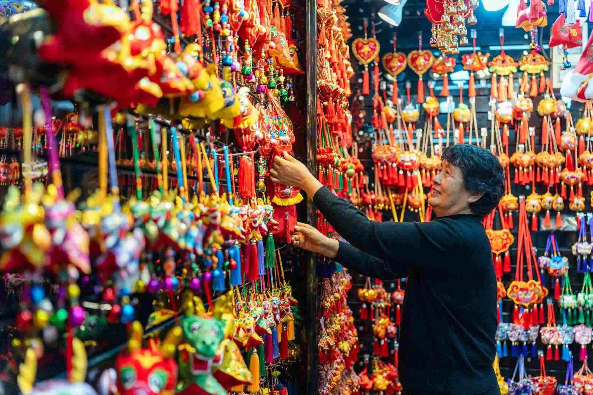 2023年12月11日，金華義烏國際商貿(mào)城，龍年喜慶用品掛滿攤位，顧客正在挑選中。