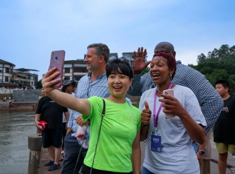 2024“一帶一路”媒體合作論壇聯(lián)合采訪調(diào)研行成員在樂(lè)山蘇稽古鎮(zhèn)與游客合影留念。本報(bào)記者 伊霄攝