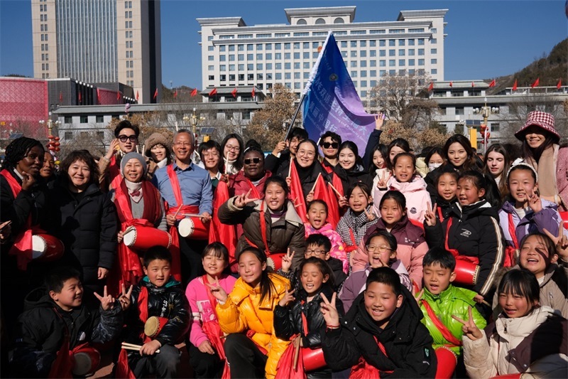 中外青年學子在安塞文化廣場觀看陜北腰鼓和大秧歌表演后合影留念，大家踏著鼓點共舞，翻飛的紅綢與躍動的身影交織，在黃土地廣場上繪出一幅生動的陜北民俗互動畫卷